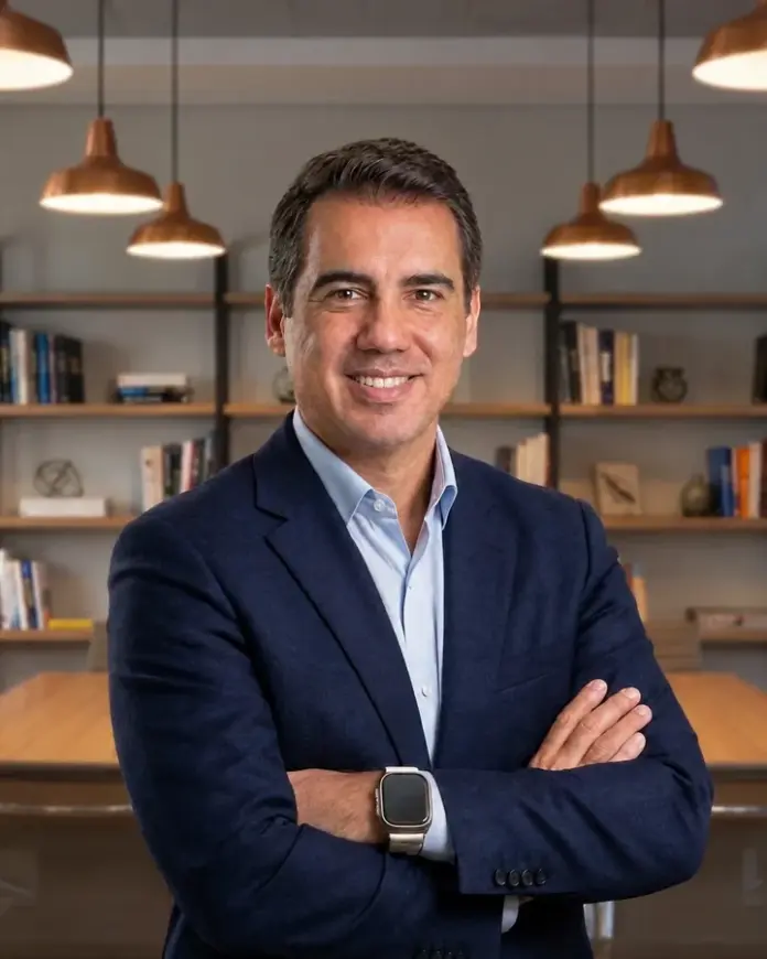 Roberto Calderon de blazer azul-marinho, braços cruzados, sorrindo no escritório